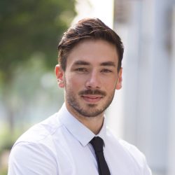 Ambitious businessman standing in street and looking at camera. Serious young manager crossing arms on chest and enjoying success. Confidence concept